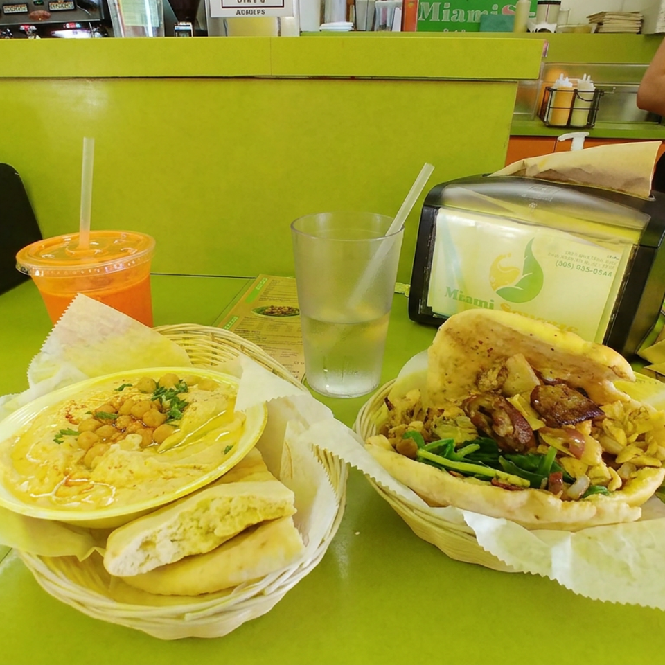 Mediterranean meal with hummus, pita bread, and a stuffed flatbread beside orange juice and water on a green restaurant table.