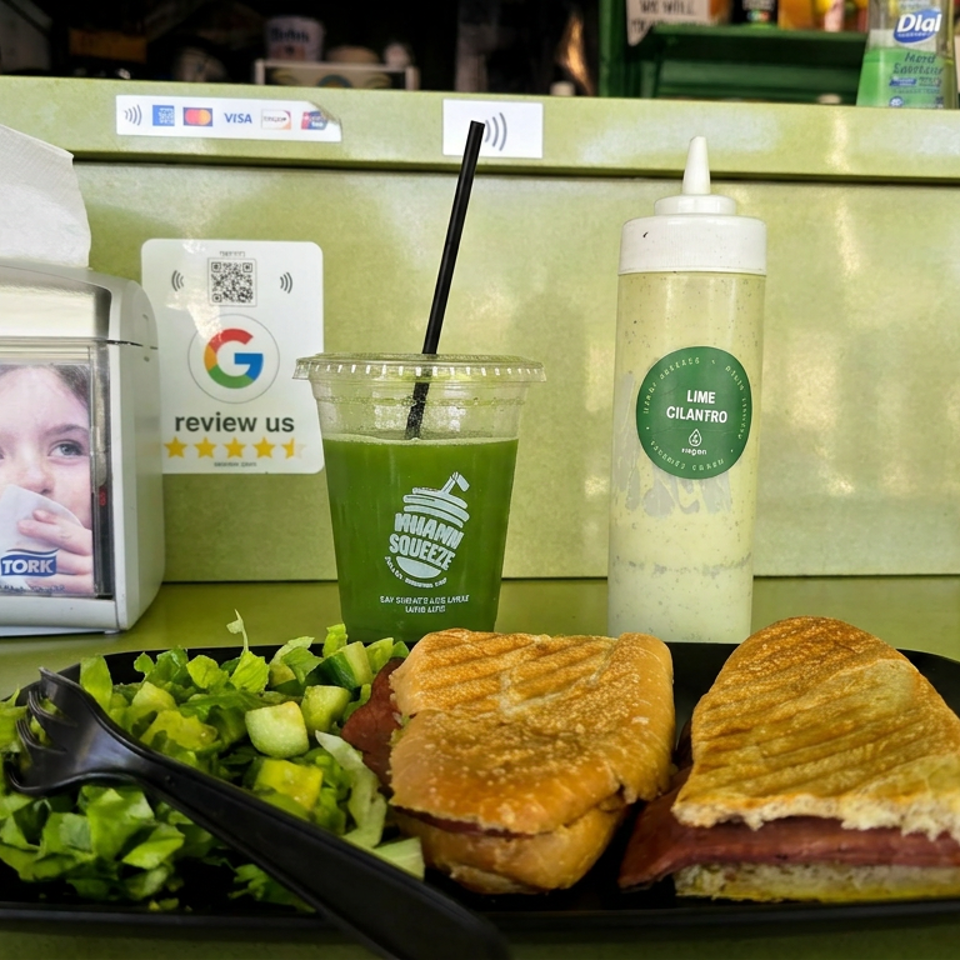 Two grilled sandwiches with salad, a green smoothie, and lime cilantro sauce on a restaurant table.