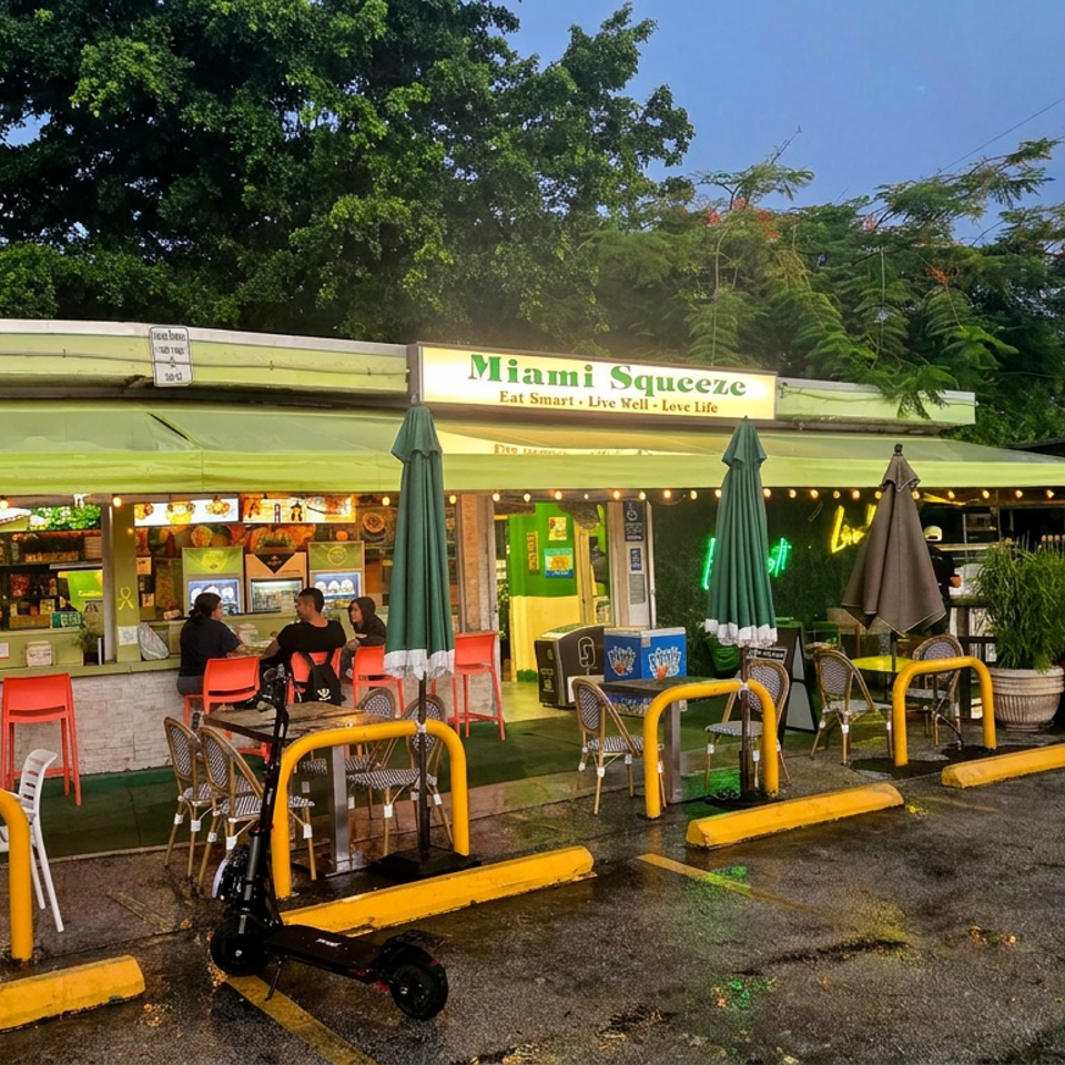 Miami Squeeze restaurant storefront with outdoor seating, umbrellas, string lights, parked cars, and a few diners.