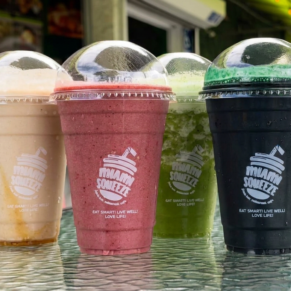 Four colorful smoothies in branded cups sit on a reflective outdoor café table.